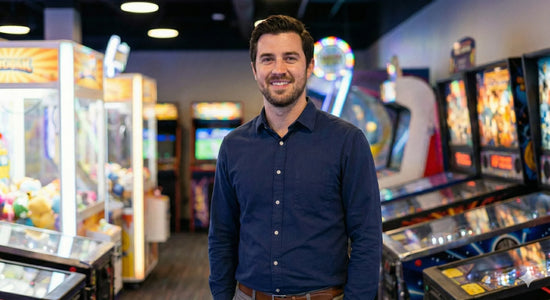 Smiling man standing in arcade with claw machines and pinball machines in background