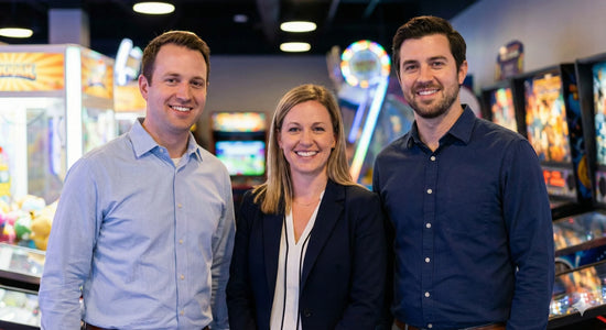 Three people smiling in an arcade with game machines in the background