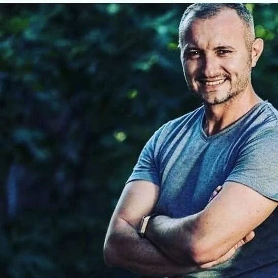 Smiling man in casual grey t-shirt standing outdoors with arms crossed